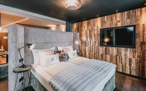 Almfeuer Modernes Hotelzimmer mit gepolstertem Bettkopfteil, Holzwand und großem Flachbildfernseher